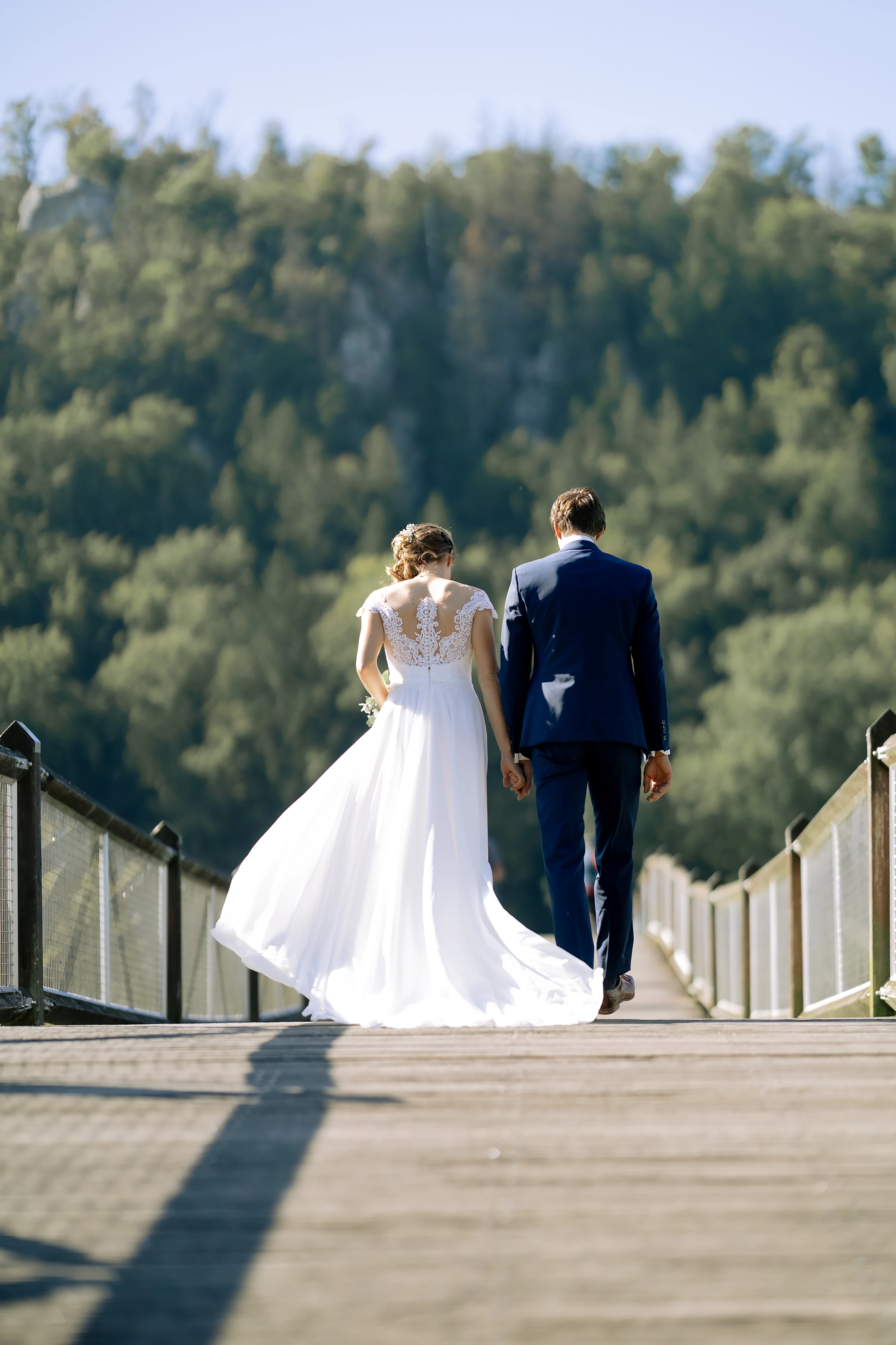 Das Brautpaar läuft auf einer Holzbrücke von der Kamera weg, das Kleid der Braut wird vom Wind gewellt.